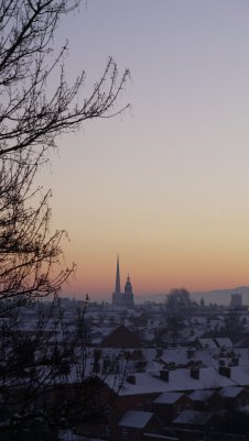 Snow covered rooftops, hazy sunset, framed to one side by the silhouette of a tree.