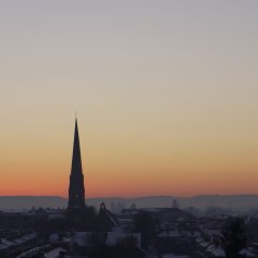 Snow covered rooftops in Worcester with a church spire silhouetted against the sunset.