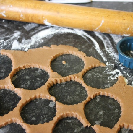 Rolled out pastry with round cut-outs on a floured surface with a rolling pin and cookie cutter.
