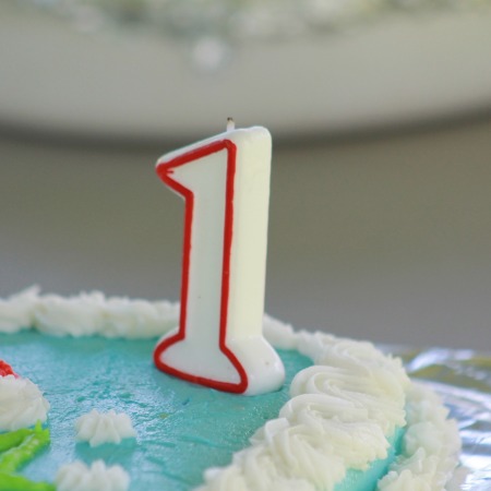 A red and white number one birthday candle on top of a blue and white iced cake.