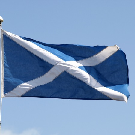 The Scottish flag flying from a flagpole against a blue sky.
