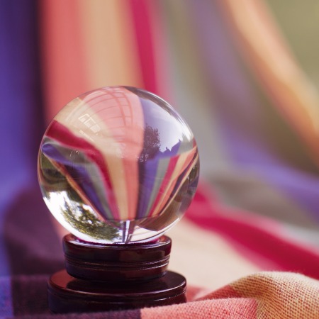 A crystal ball on a wooden stand against a purple and pink cloth background.