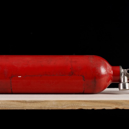An old red, unlabelled fire extinguisher, lying on its side on a wooden table.