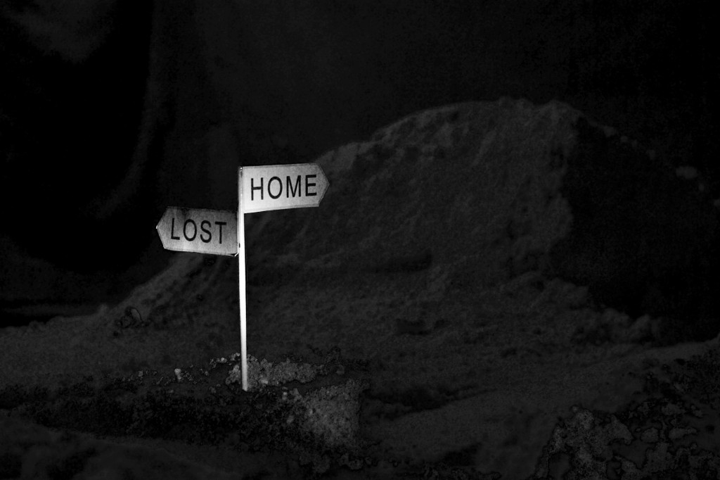 Dark almost invisible landscape. White signpost in foreground. Left sign points to 'Lost'. Right sign points to 'Home'.